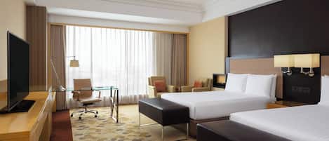 A hotel room with two beds, a desk with a TV, a chair, a small table, and a large window with curtains.