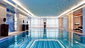 Una piscina interior moderna con piso de vidrio, ventanas amplias e iluminación contemporánea.