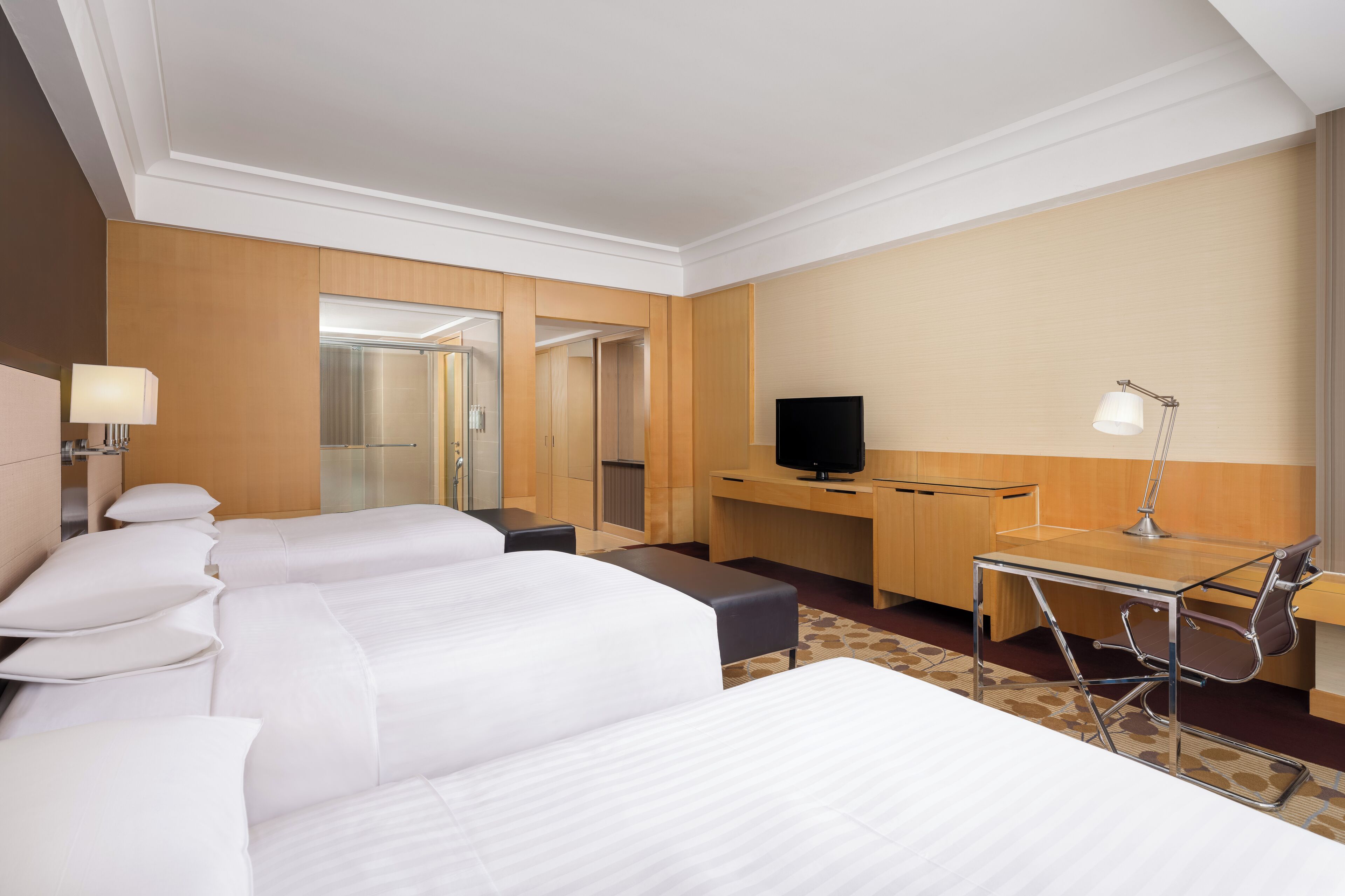 A hotel room with two beds, a desk, a TV, and a lamp.