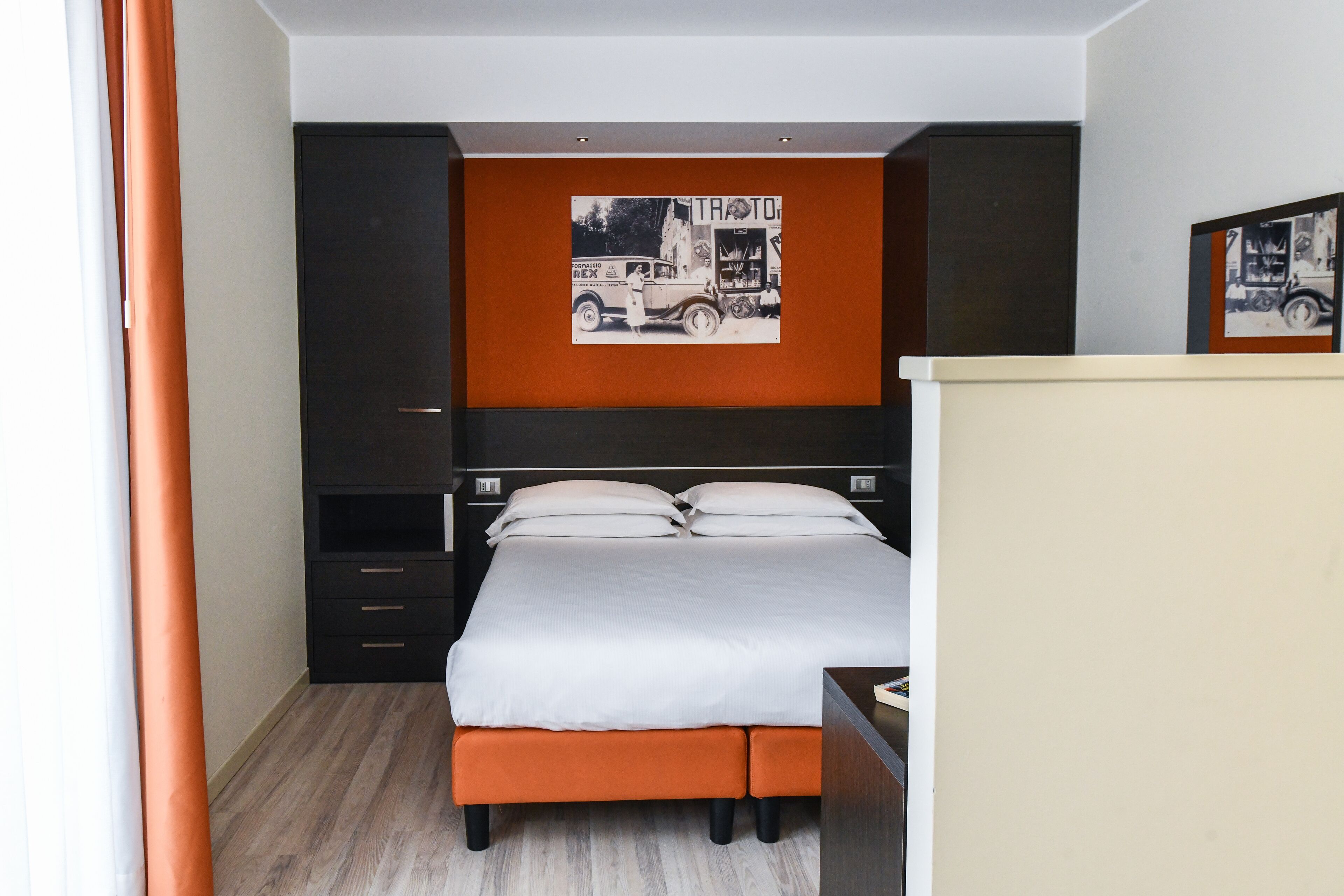 A bedroom with a bed, a nightstand, a dresser, and a wall-mounted artwork.