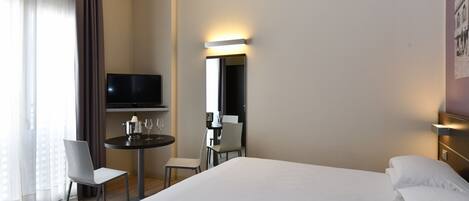 A hotel room with a bed, a desk with a chair, a television, and a mirror.