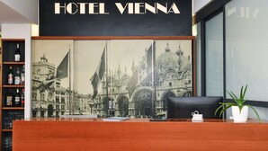 A reception desk with a large framed historical cityscape photograph, a sign reading "HOTEL VIENNA," and a potted plant. - Hotel Vienna (Jesolo)