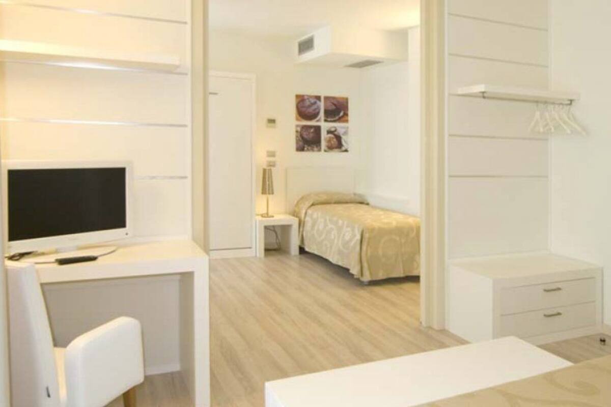 A bedroom with a bed, a desk, a chair, and a TV.