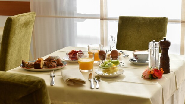 A breakfast table set with plates of food, a glass of orange juice, and a cup of coffee. - Hotel Vienna (Jesolo)