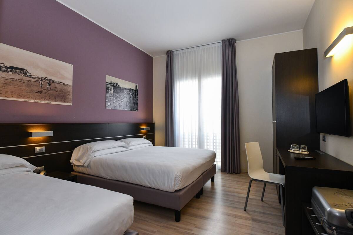 A hotel room with two beds, a desk with a chair, a television, and artwork on the walls.