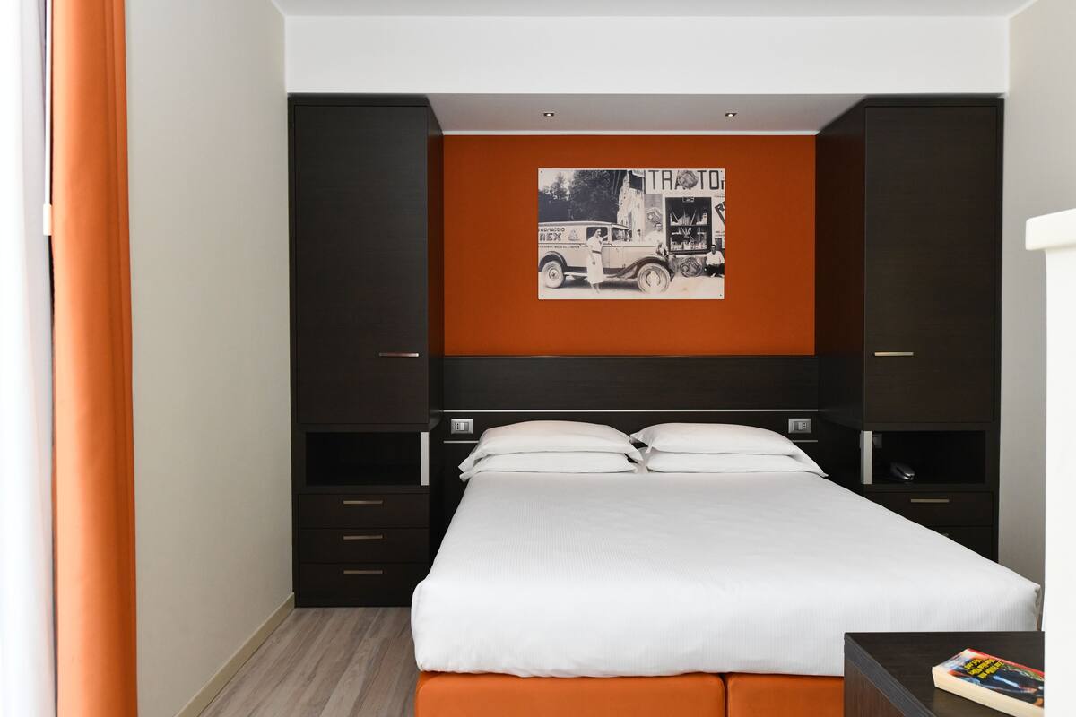 A modern hotel room with a large bed, dark wood furniture, and a wall-mounted artwork depicting a vintage truck.