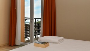 A hotel room with a bed, a book, and a view of a balcony with orange curtains. - Hotel Vienna (Jesolo)