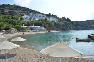 A beach with umbrellas, a boat, and a building with a white facade on a hillside.