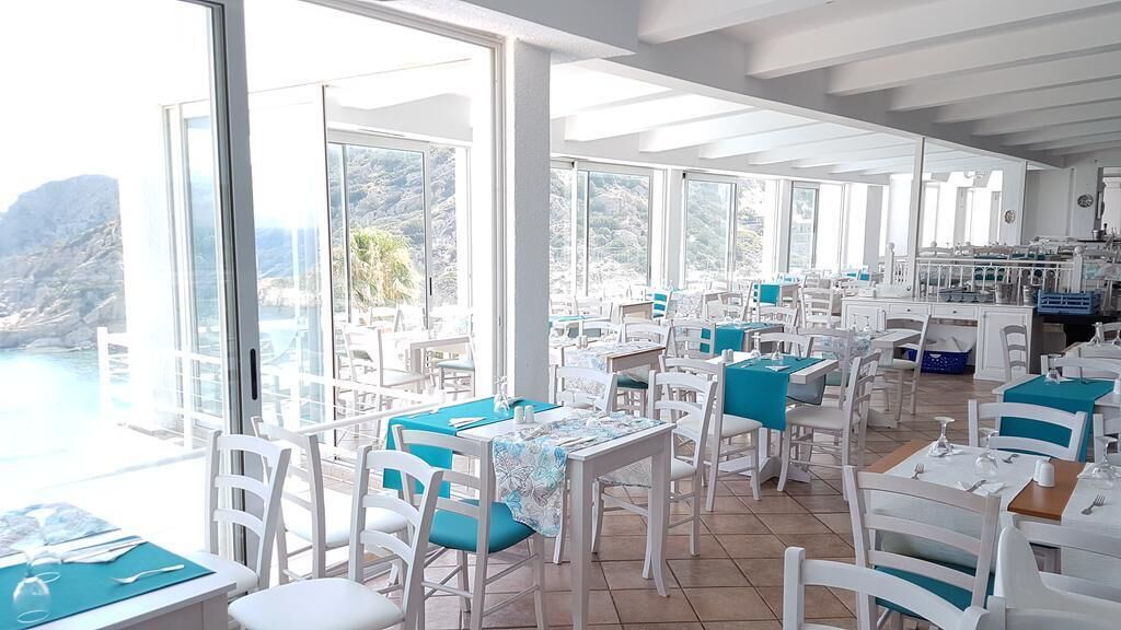 A restaurant with white chairs and tables, large windows, and a view of the sea.