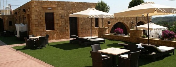 An outdoor patio with stone walls, wicker furniture, and white umbrellas.