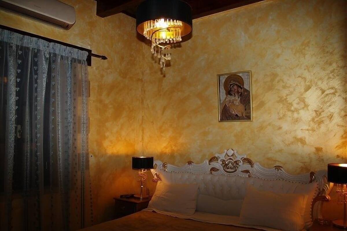 Une chambre à coucher avec un lit, un lustre, un tableau accroché au mur et une fenêtre avec des rideaux.