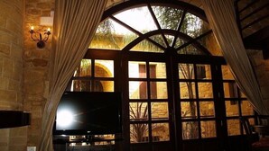 A room with a stone wall, a large arched window, and a flat-screen TV. - Palazzo Loupassi Villas (Platanias)