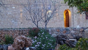 A stone building with a wooden door and a garden with rocks and flowers. - Palazzo Loupassi Villas (Platanias)