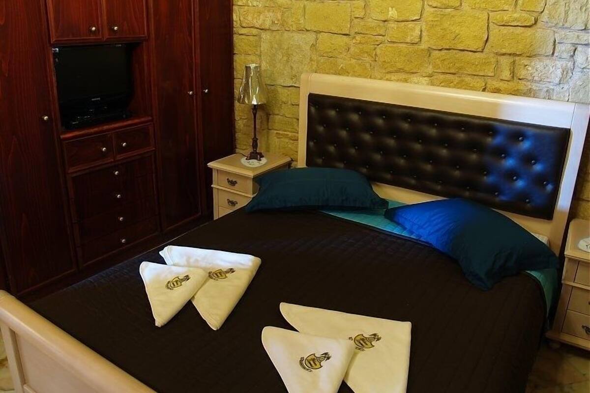 Une chambre d’hôtel avec un lit, une télévision, une table de chevet et un mur en pierre.