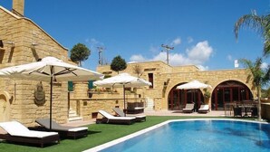 A pool area with lounge chairs and umbrellas, stone walls, and a clear blue sky. - Palazzo Loupassi Villas (Platanias)