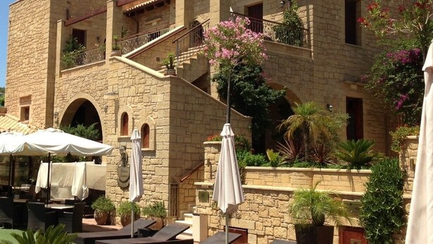 A poolside area with lounge chairs and umbrellas, a stone building with balconies, and a clear sky. - Palazzo Loupassi Villas (Platanias)