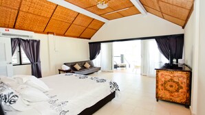 Quarto de hotel com uma cama grande, um sofá, uma escrivaninha e uma porta de vidro deslizante que dá para uma varanda.