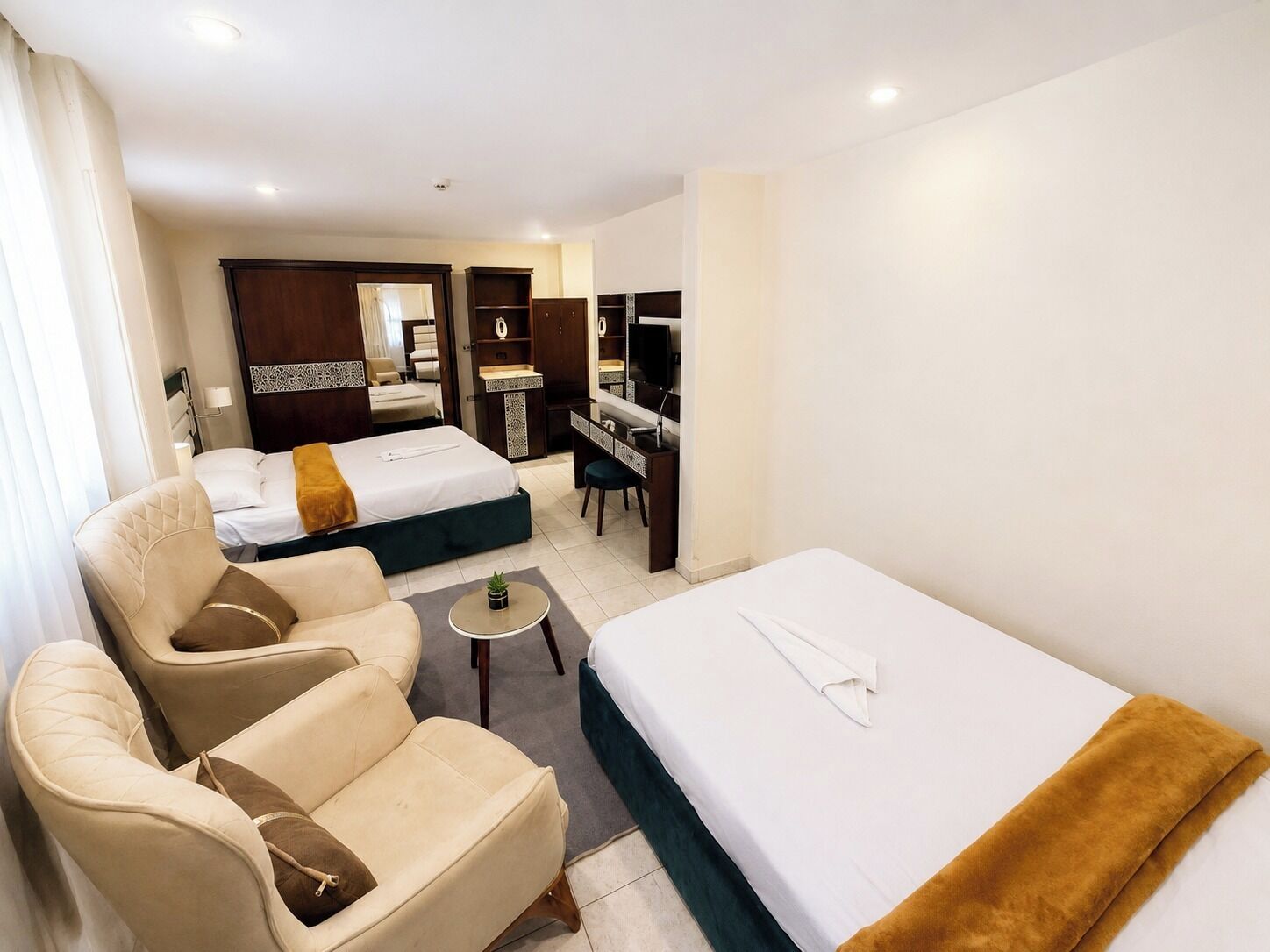 A hotel room with two beds, a sofa, a desk, and a TV.