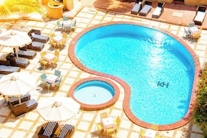 Una piscina con tumbonas y sombrillas, rodeada por un patio empedrado.