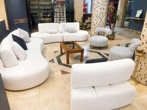 Uma sala de estar moderna com sofás brancos, uma mesa de centro de vidro e pufes estampados.