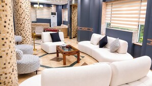 A modern living room with a sofa set, a coffee table, patterned ottomans, and a decorative chandelier. - Karnak Hotel Luxor (Luxor)