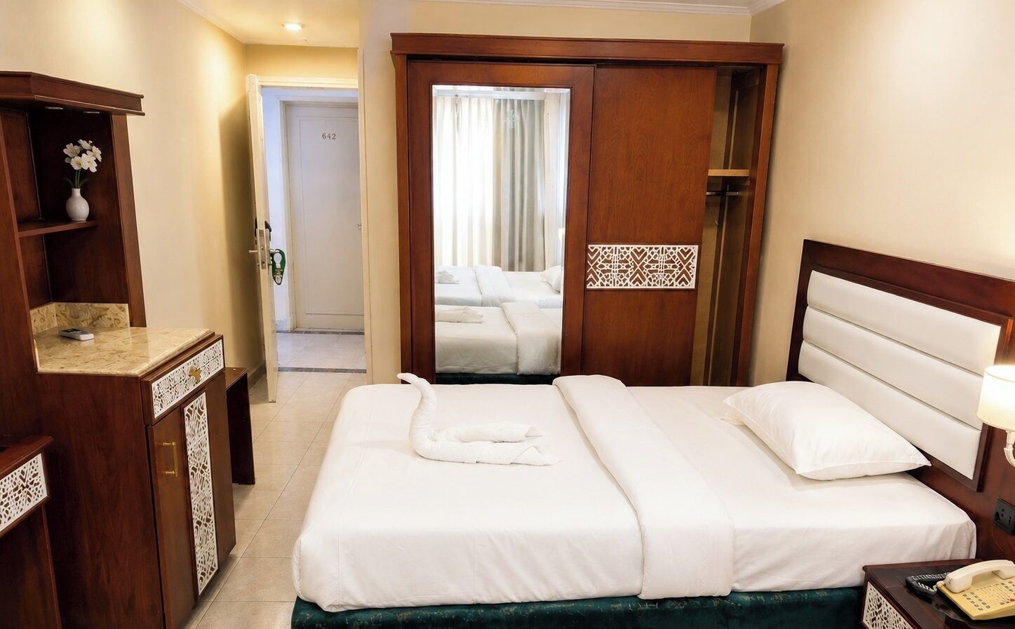 A hotel room with a bed, a nightstand, a wooden wardrobe, and a bathroom visible through an open door.
