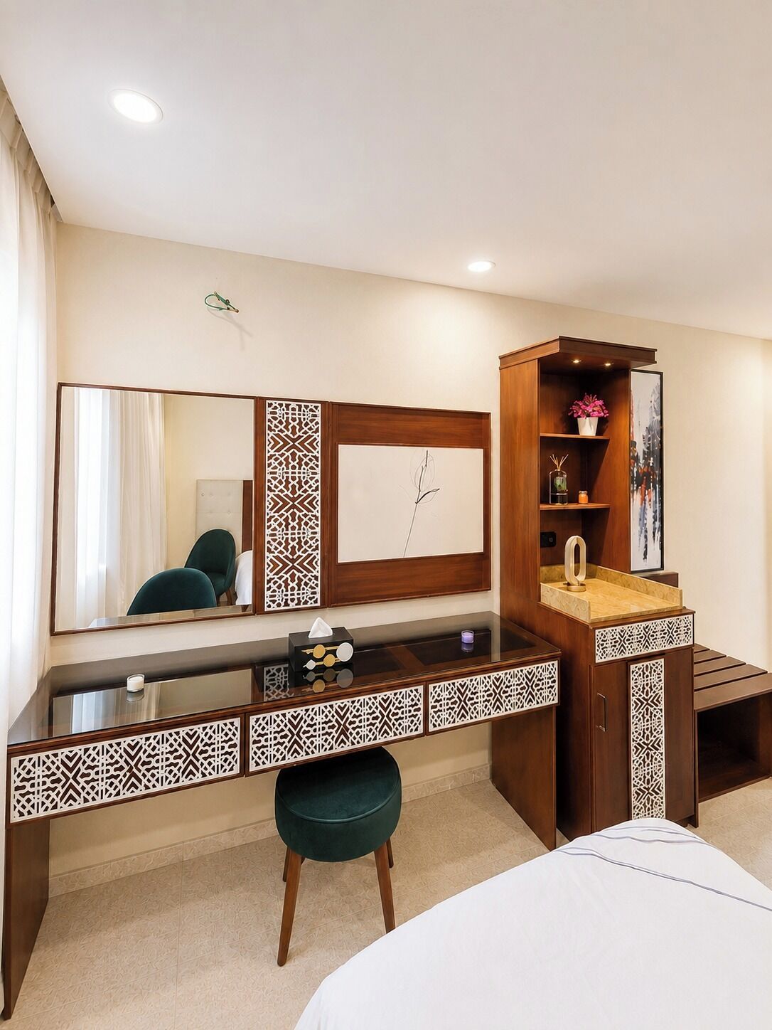 Une chambre d’hôtel avec un grand miroir, un bureau en bois, une chaise verte, un lit et une petite armoire contenant des objets décoratifs.