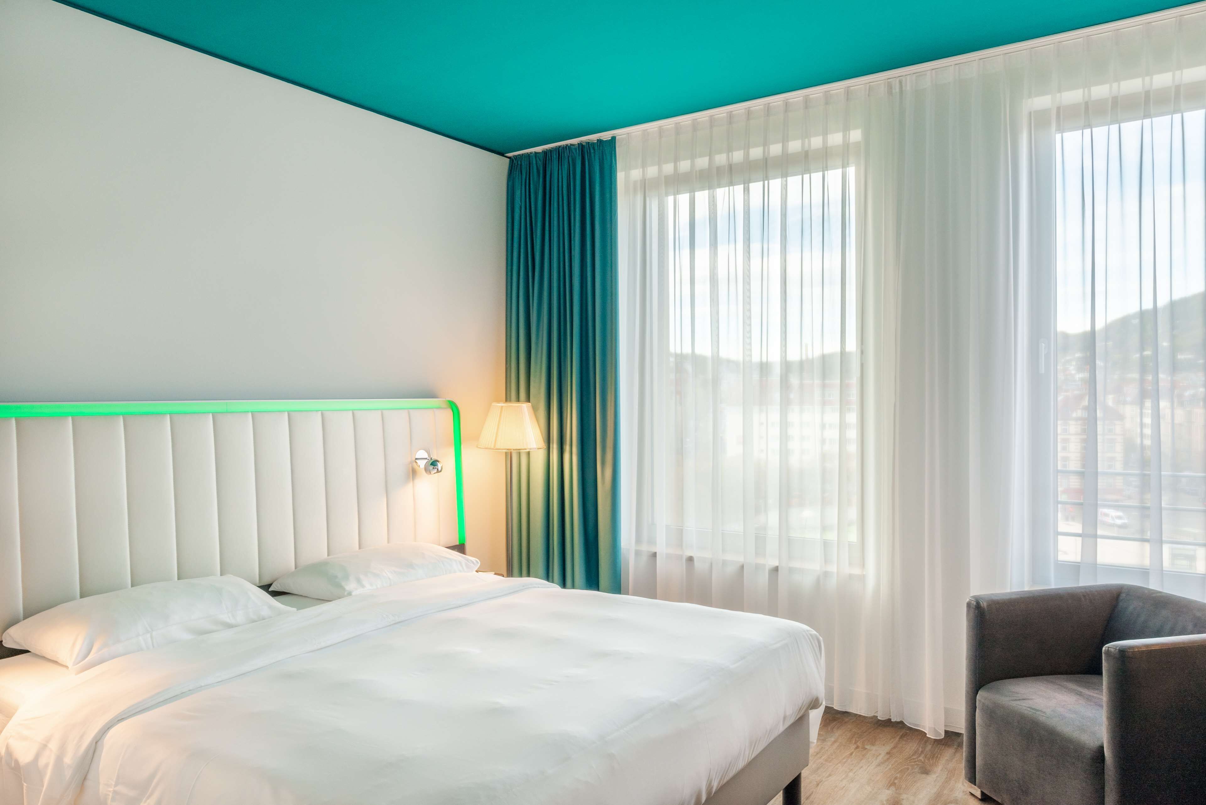 Habitación de hotel con cama, una silla, ventana con cortinas y vistas al exterior.