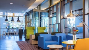 A modern lobby with blue and yellow seating, large windows, and a red striped carpet. - Park Inn by Radisson Stuttgart (Stuttgart)