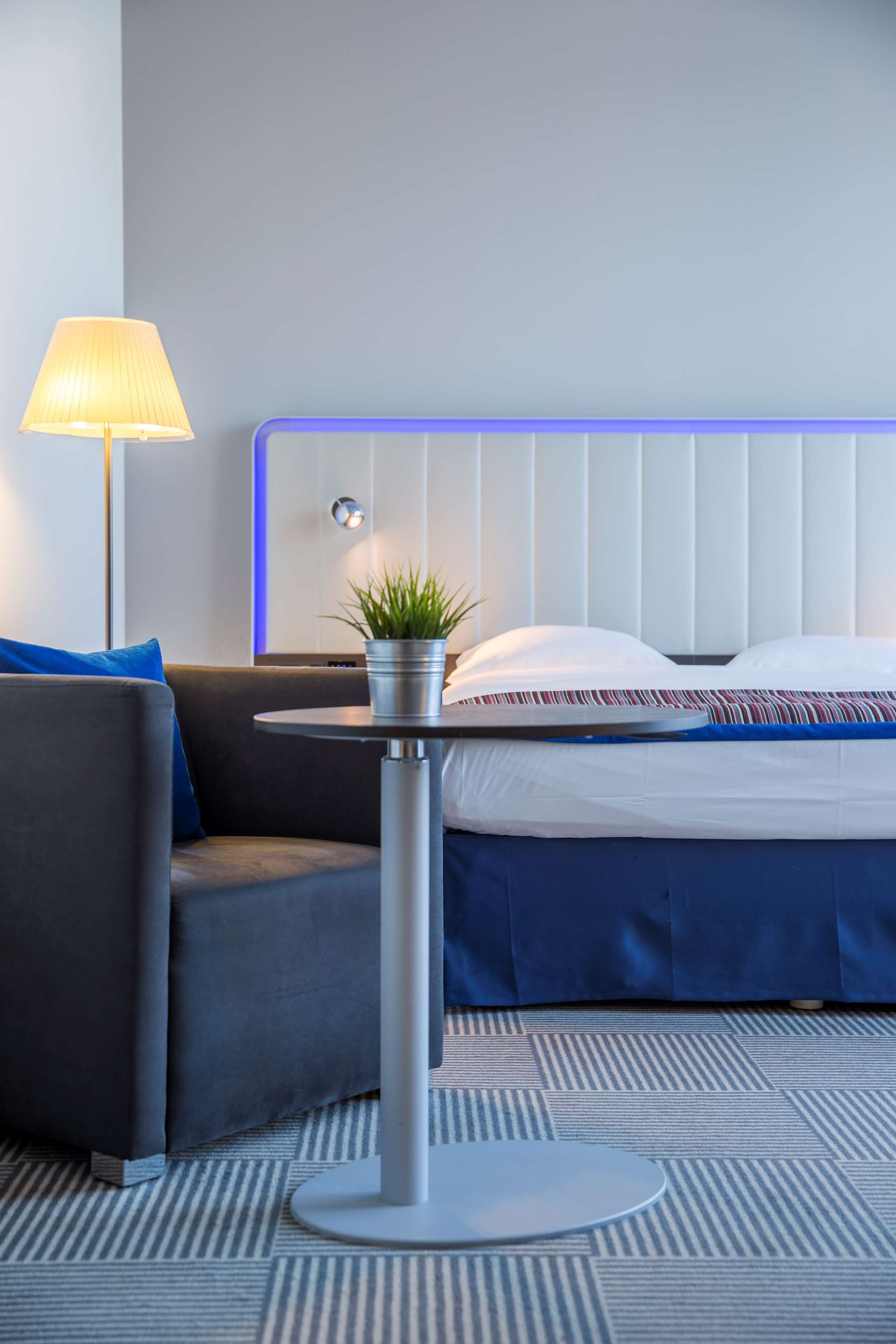 Ein modernes Hotelzimmer mit Bett, einem runden Tisch mit Pflanze, einer Lampe und einem Sofa.
