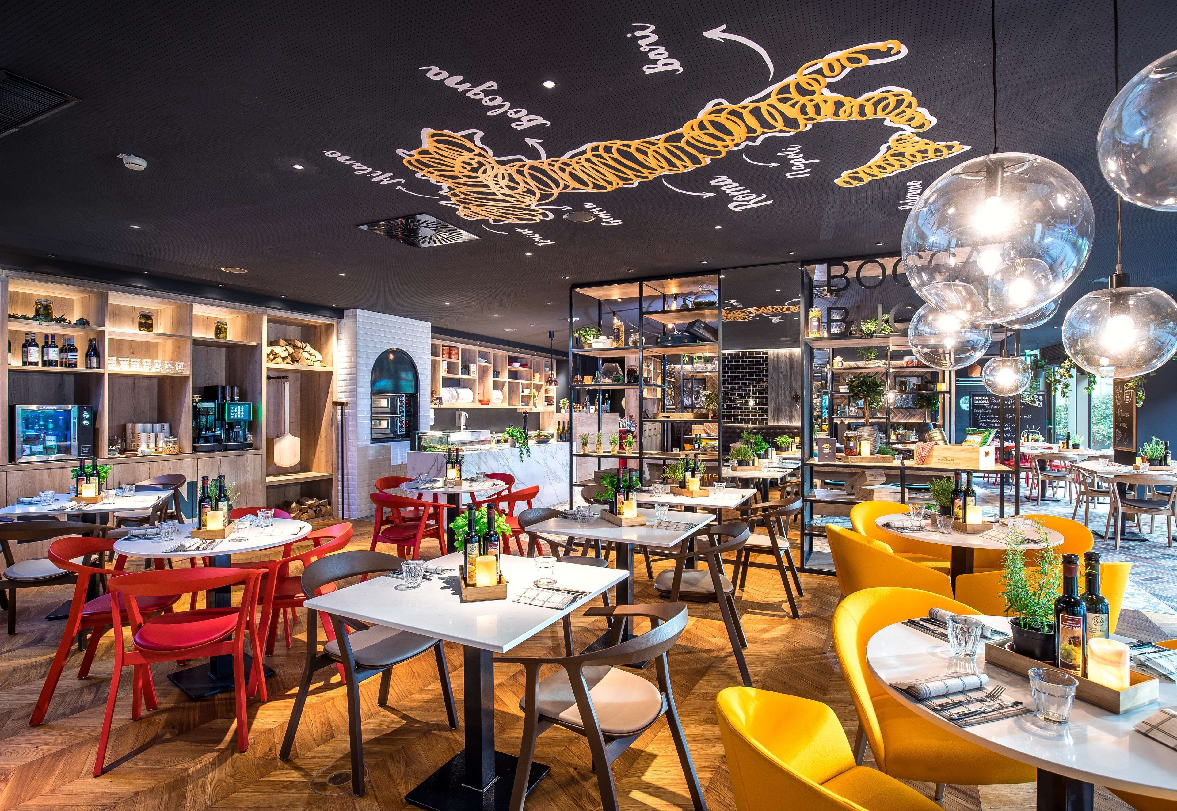 Un restaurante con mesas, sillas, una zona de cocina y estantes con botellas.