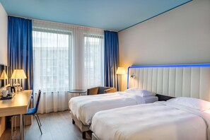A hotel room with two beds, a desk, a chair, and a small table.
