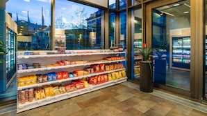 A grocery store with shelves stocked with snacks and beverages, large windows, and a potted plant. - Park Inn by Radisson Stuttgart (Stuttgart)