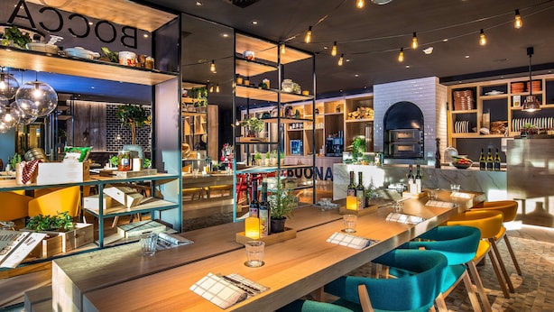 A restaurant with wooden tables, blue chairs, and a bar area with shelves and bottles. - Park Inn by Radisson Stuttgart (Stuttgart)
