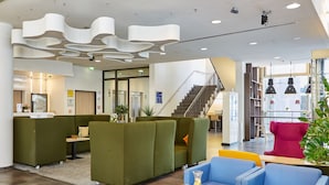 A modern lobby with green and blue seating, a staircase, and a large window with a view. - Park Inn by Radisson Stuttgart (Stuttgart)
