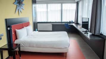 Habitación de hotel con cama, escritorio, silla, televisor y ventana con cortinas.
