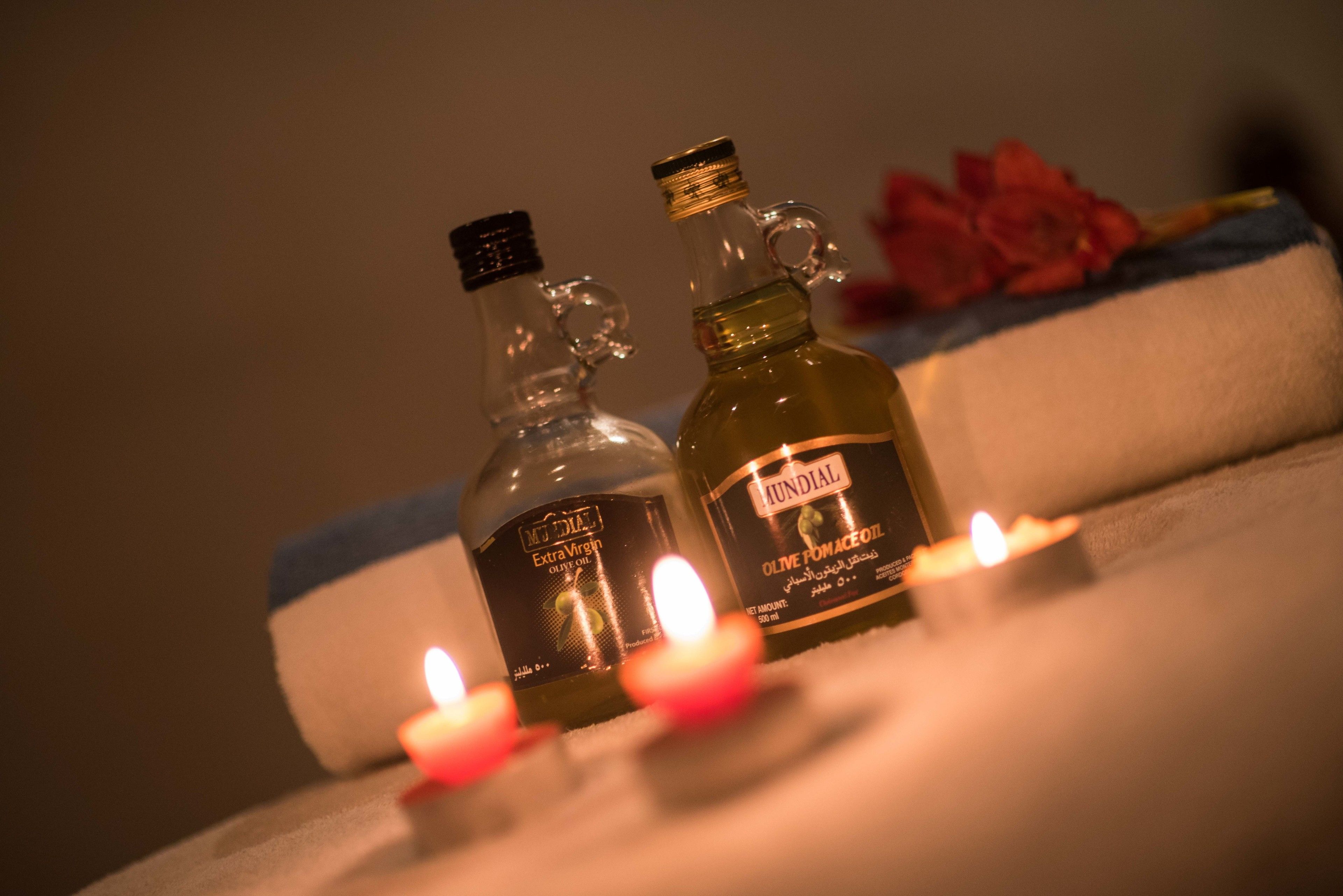 Two bottles of olive oil on a table with candles.