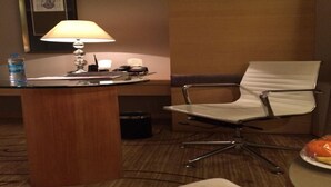 A hotel room with a wooden desk, a white chair, a lamp, a water bottle, and a plate with food. - Xinhua Jianguo Hotel Jiujiang (Jiujiang)