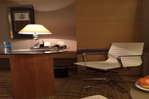 A hotel room with a wooden desk, a white chair, a lamp, a water bottle, and a plate with food. - Xinhua Jianguo Hotel Jiujiang (Jiujiang)