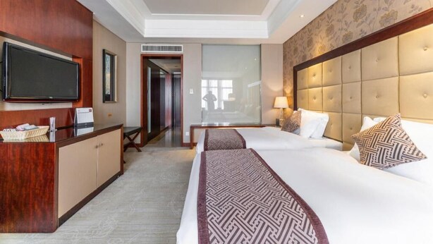 A hotel room with a large bed, a desk with a flat-screen TV, a minibar, and a large window. - Xinhua Jianguo Hotel Jiujiang (Jiujiang)