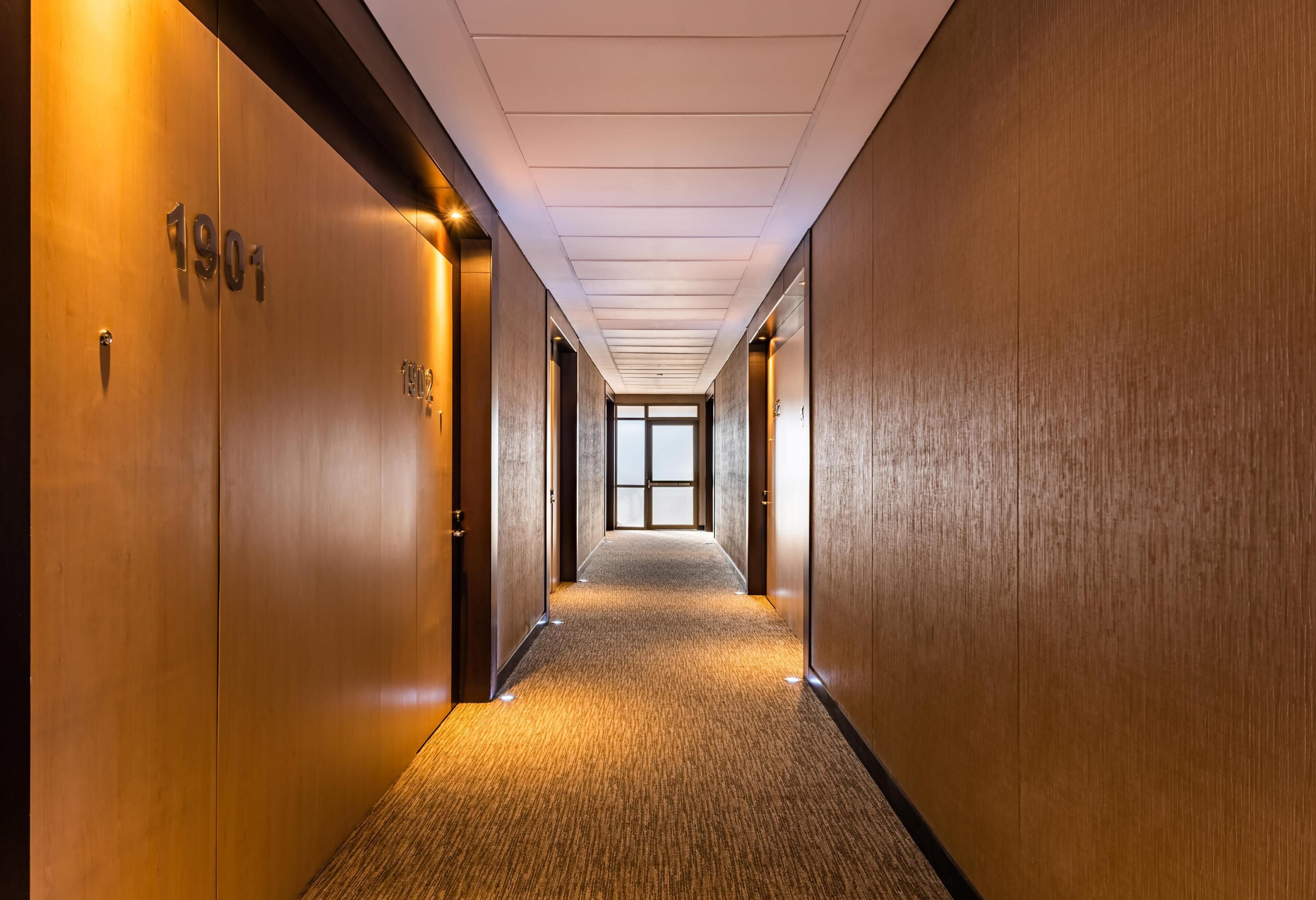 Un largo pasillo estrecho con paredes de madera y pisos alfombrados, que conduce a una puerta de vidrio grande al final.