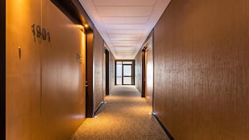 Un largo pasillo estrecho con paredes de madera y pisos alfombrados, que conduce a una puerta de vidrio grande al final.