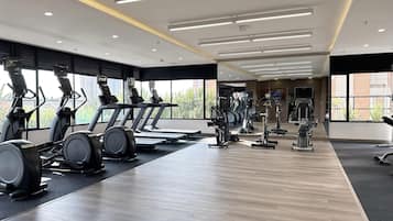 Une salle de sport moderne équipée de divers appareils de cardio, d’un mur avec des miroirs et de grandes fenêtres donnant sur un paysage verdoyant.