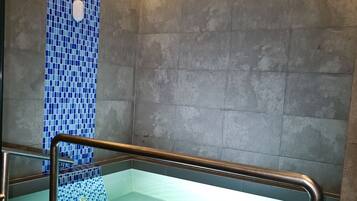 Un baño moderno con ducha acristalada, paredes de azulejos y una escalera de madera.