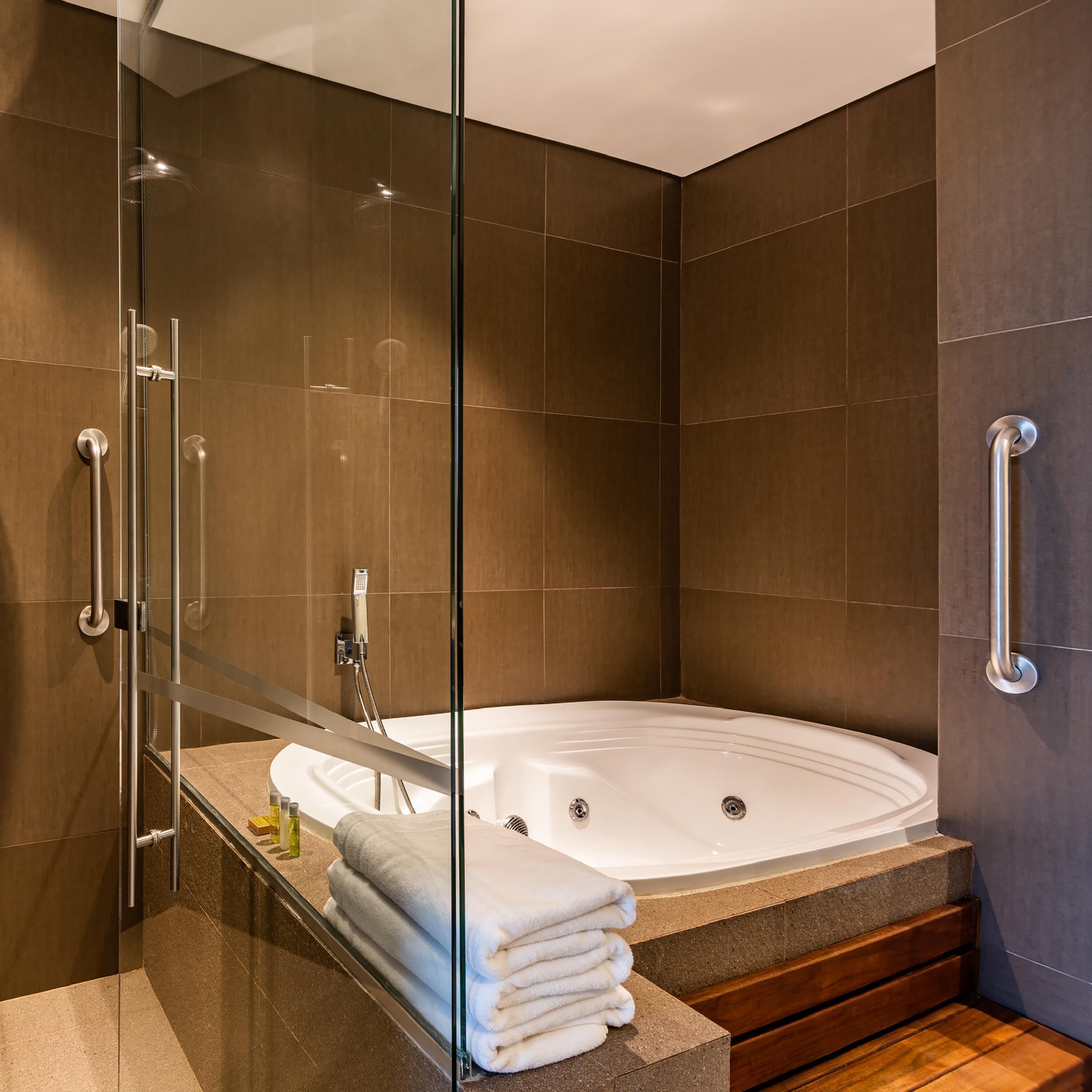 Un baño moderno con ducha de vidrio, bañera blanca y banco de madera.