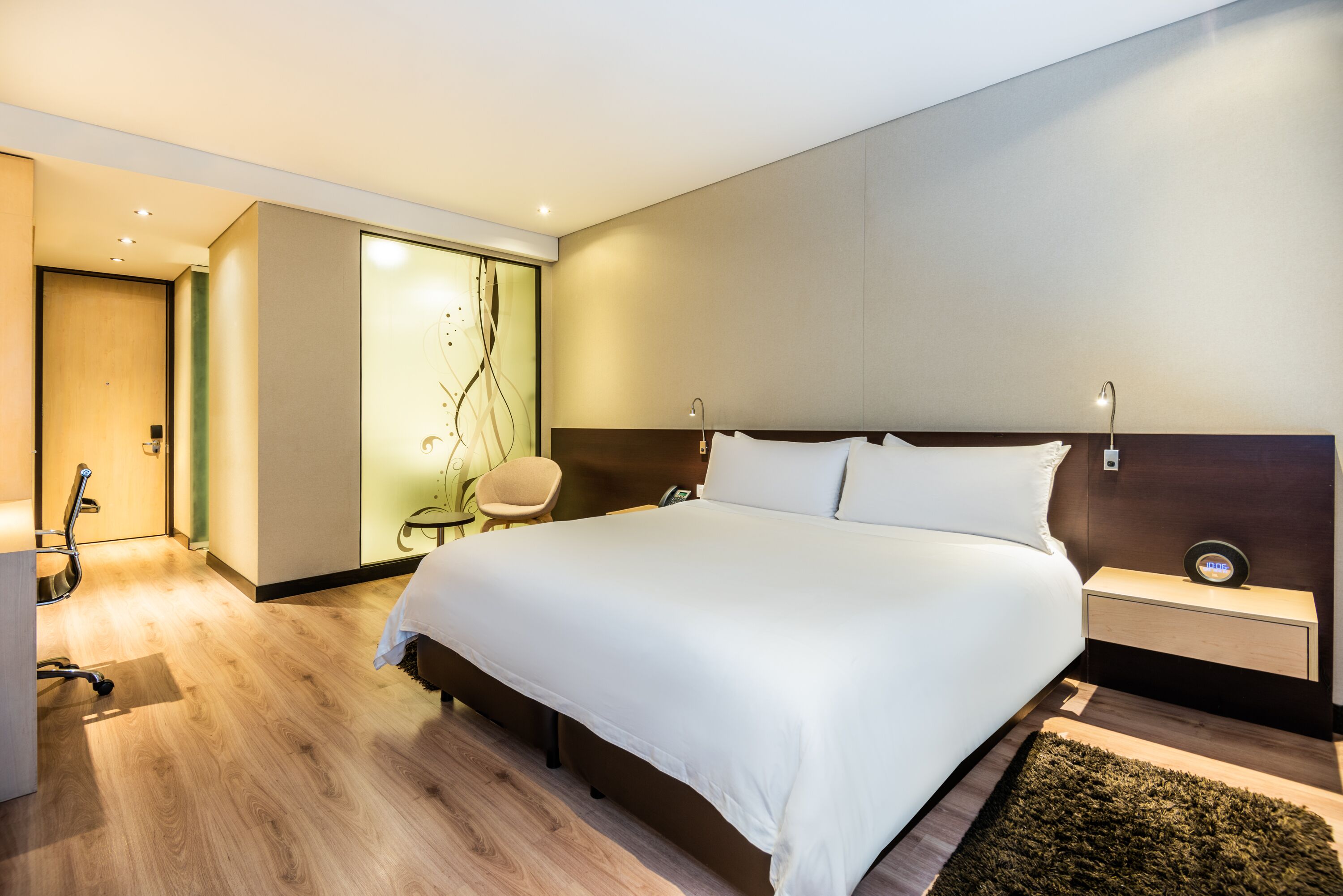 Quarto de hotel moderno com uma cama grande, mesa de cabeceira e uma cadeira.