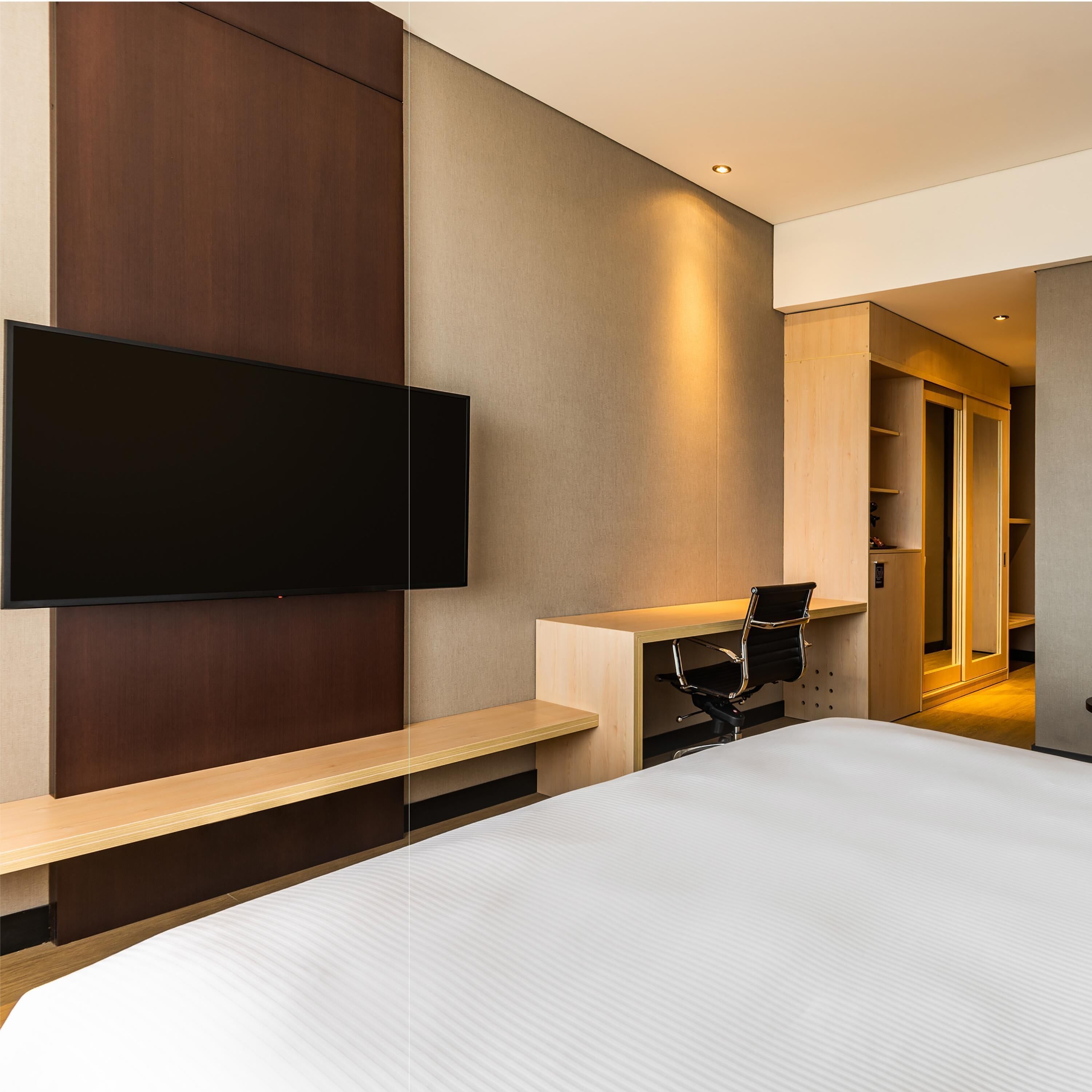 Una habitación de hotel moderna con una cama grande, un televisor de pantalla plana montado en la pared, un escritorio con una silla y un vestidor.