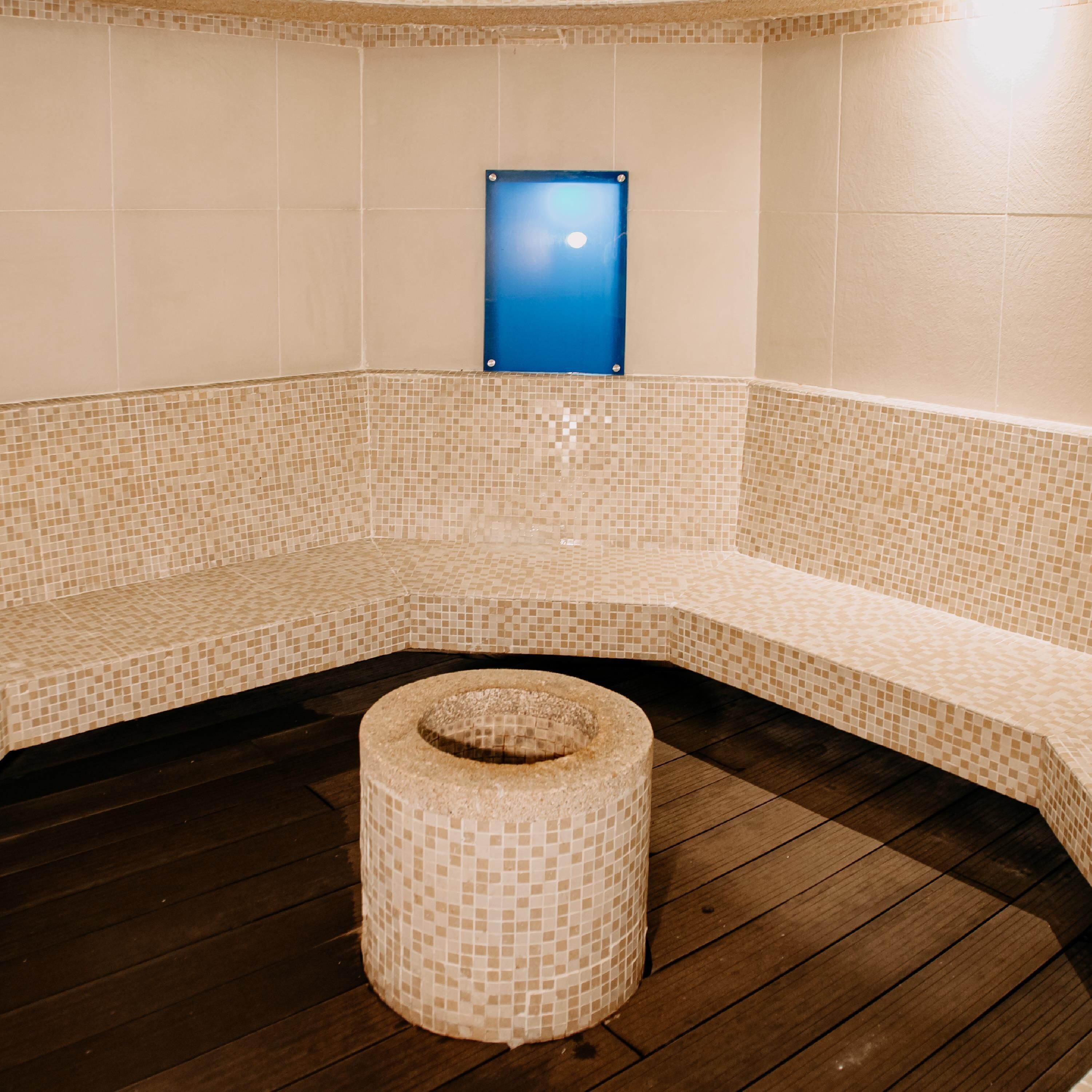 Een spa ruimte met een bank met mozaïektegels, een rond krukje en een blauw bord aan de muur.