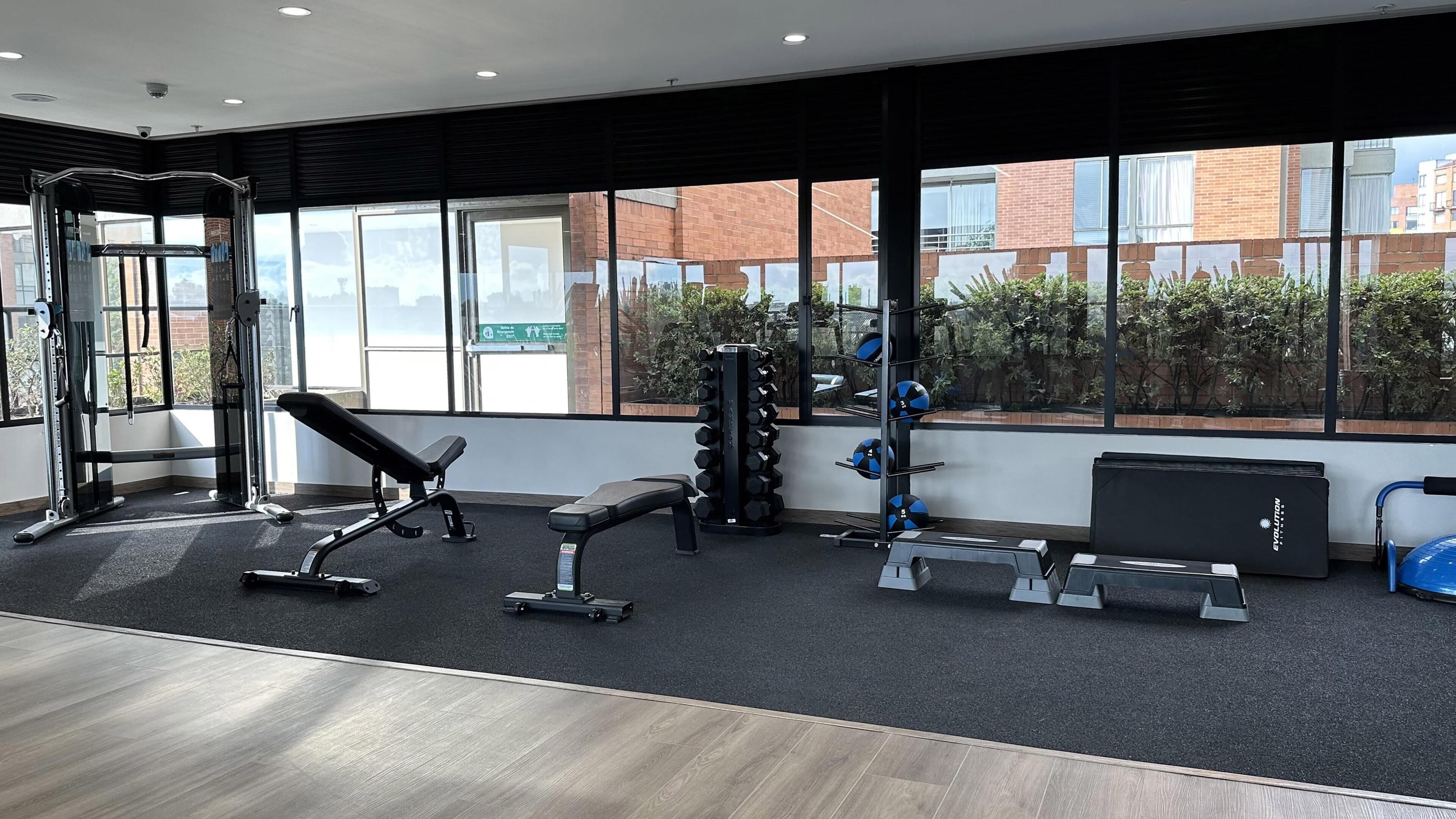 A gym with exercise equipment, large windows, and a view of buildings and greenery.