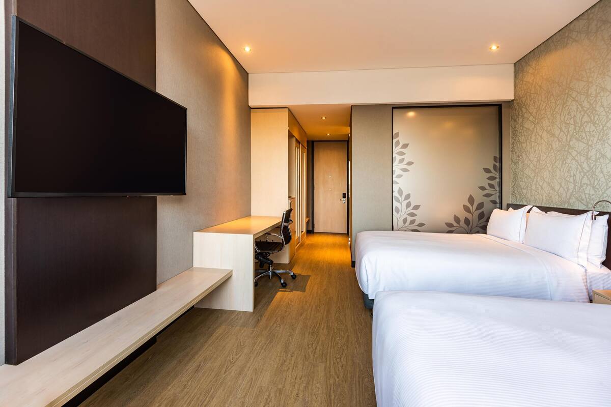 A hotel room with a bed, a desk, a chair, a TV, and a wardrobe.